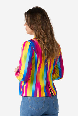 Image of woman wearing vertically striped rainbow colored women's blazer , white shirt and blue jeans. She is holding the sides of the blazer. View from the back.