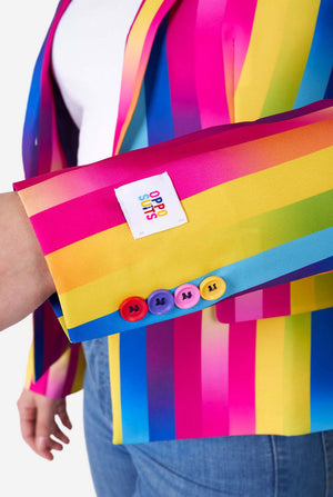Close-up image of woman wearing vertically striped rainbow colored women's blazer , white shirt and blue jeans. She is showing the sleeve with colored buttons.