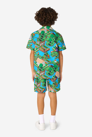 A young boy wearing a colorful summer outfit featuring a Minecraft Overworld print, showcasing pixelated landscapes, characters, and elements from the iconic game. The short-sleeve shirt and matching shorts highlight a vibrant design inspired by the Minecraft universe. View from the back.