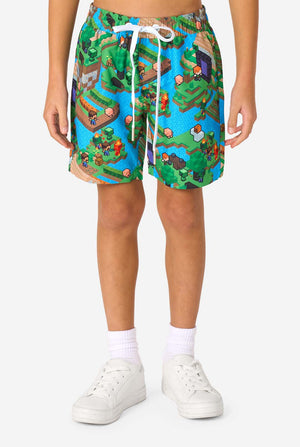 A young boy wearing a colorful summer outfit featuring a Minecraft Overworld print, showcasing pixelated landscapes, characters, and elements from the iconic game. The short-sleeve shirt and matching shorts highlight a vibrant design inspired by the Minecraft universe. Close-up shorts.