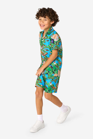 A young boy wearing a colorful summer outfit featuring a Minecraft Overworld print, showcasing pixelated landscapes, characters, and elements from the iconic game. The short-sleeve shirt and matching shorts highlight a vibrant design inspired by the Minecraft universe. Walking