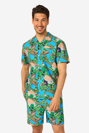 A man wearing a colorful summer outfit featuring a Minecraft Overworld print, showcasing pixelated landscapes, characters, and elements from the iconic game. The short-sleeve shirt and matching shorts highlight a vibrant design inspired by the Minecraft universe.