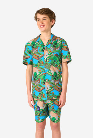 A Teen boy wearing a colorful summer outfit featuring a Minecraft Overworld print, showcasing pixelated landscapes, characters, and elements from the iconic game. The short-sleeve shirt and matching shorts highlight a vibrant design inspired by the Minecraft universe.