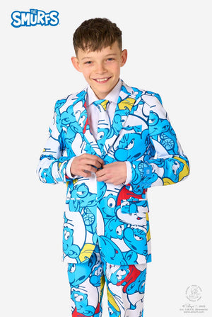 Teen boy wearing a vibrant Smurfs kids suit with colorful cartoon character prints in blue, red, yellow, and white, paired with a matching tie and white shirt, smiling against a plain background.