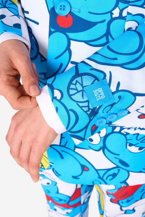 Teen boy wearing a vibrant Smurfs kids suit with colorful cartoon character prints in blue, red, yellow, and white, paired with a matching tie and white shirt, smiling against a plain background. Sleeves close up.