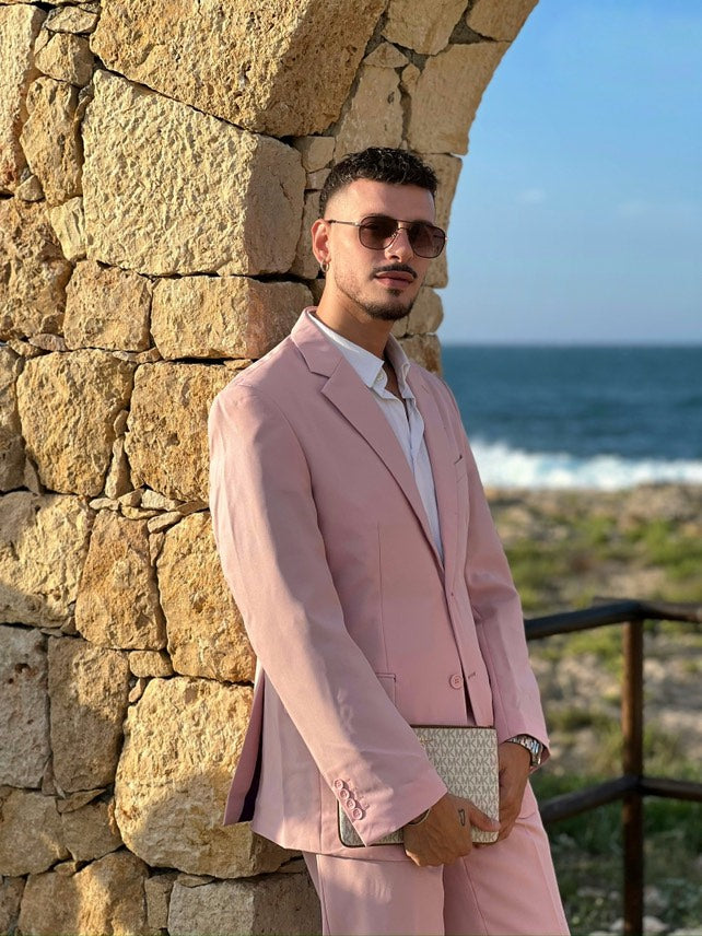Man in a pink suit standing against a stone wall with ocean view