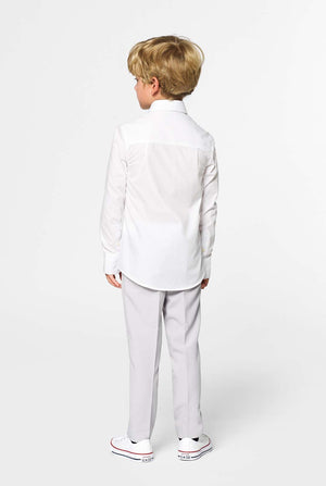 Kid standing with his back to the camera in front of a white background. Kis is wearing a white boys shirt and grey pants. Looking sideways.