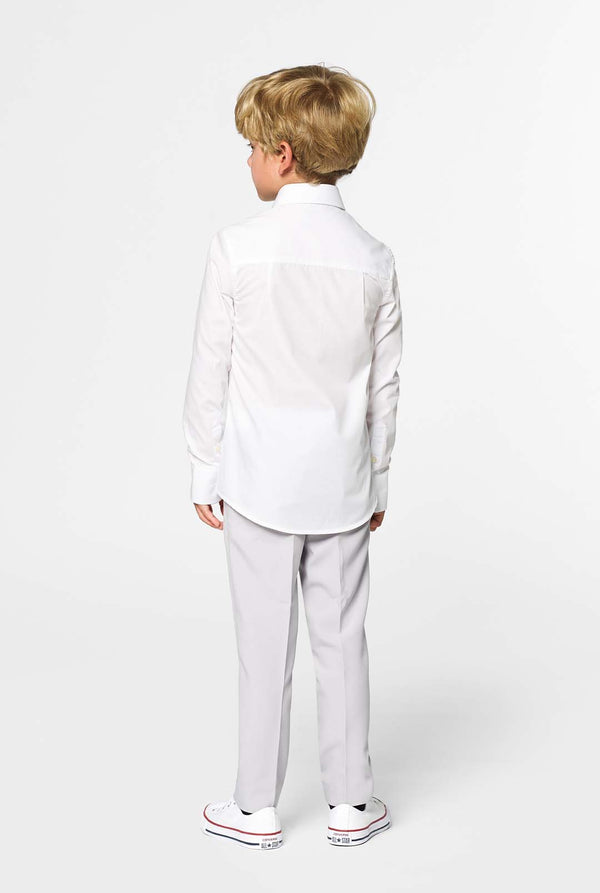 Kid standing with his back to the camera in front of a white background. Kis is wearing a white boys shirt and grey pants. Looking sideways.