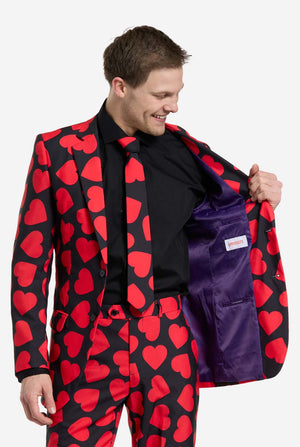Man wearing a red heart patterned suit with a purple pocket square on a white background