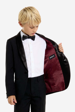 Young boy in a formal black suit with a bow tie holding a matching jacket.