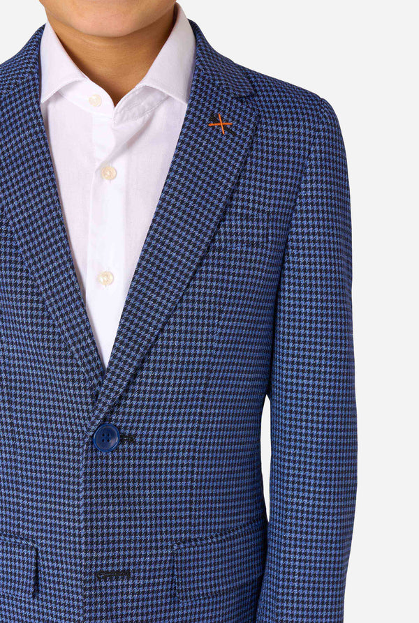 A boy wearing a navy and blue checkered suit with a white dress shirt. The suit has a modern fit with two buttons and flap pockets. He stands against a plain white background. Close up of the chest