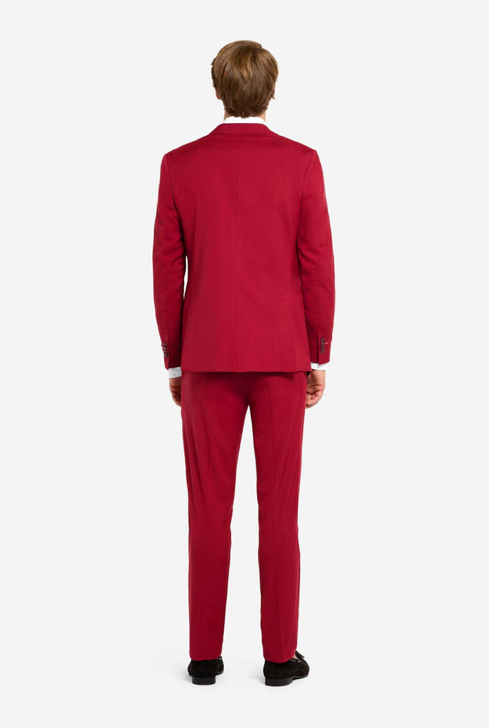 Image with light grey background and man wearing Bright Burgundy men’s suit and white shirt. Suits consists of blazer and pants. View from the back.