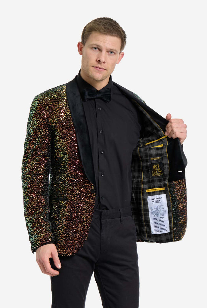 This image showcases a stylish men’s dinner jacket from OppoSuits Deluxe collection, featuring dazzling amber sequins that create a shimmering effect. The sequin blazer has a sleek satin lapel, a tailored fit. The model pairs it with a classic black dress shirt and bow tie, making this jacket perfect for formal events, holiday parties, or New Year celebrations. Ideal for men who want to stand out with bold, luxurious, and festive attire. Holding a side of the jacket open.