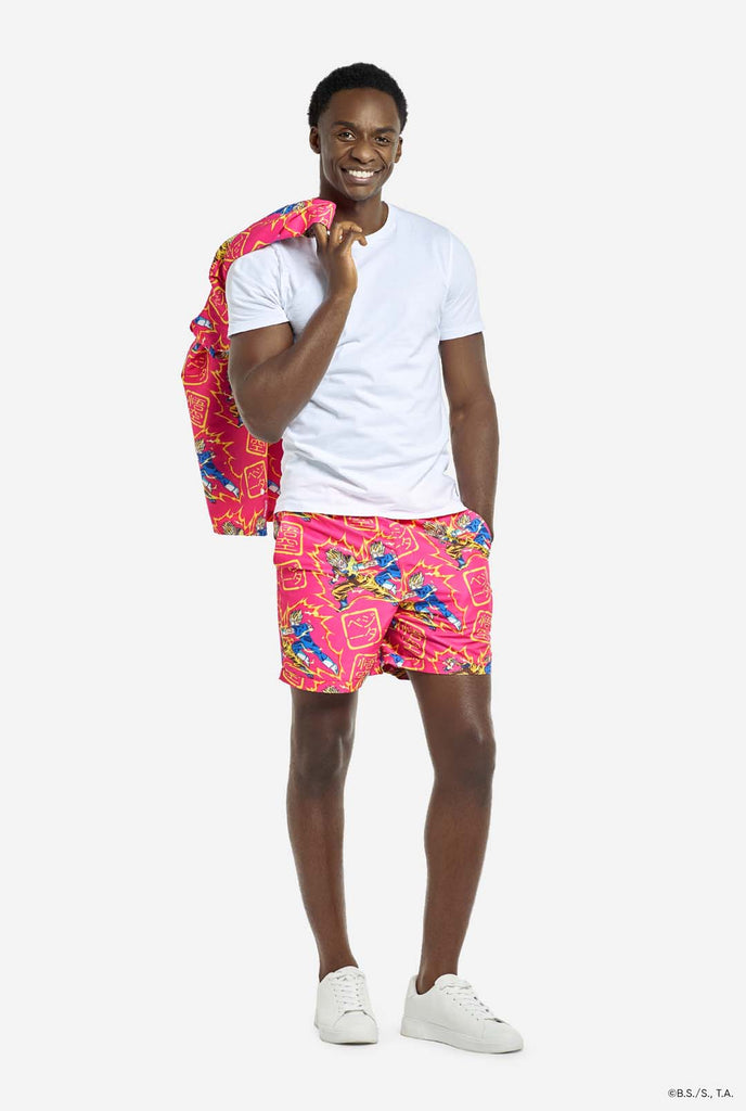 Man wearing pink summer set consisting of shirts and shorts. Summer set has Dragon Ball Z Goku and Vegeta fighting print. He is holding the shirt over his shoulder and wearing a white t-shirt.