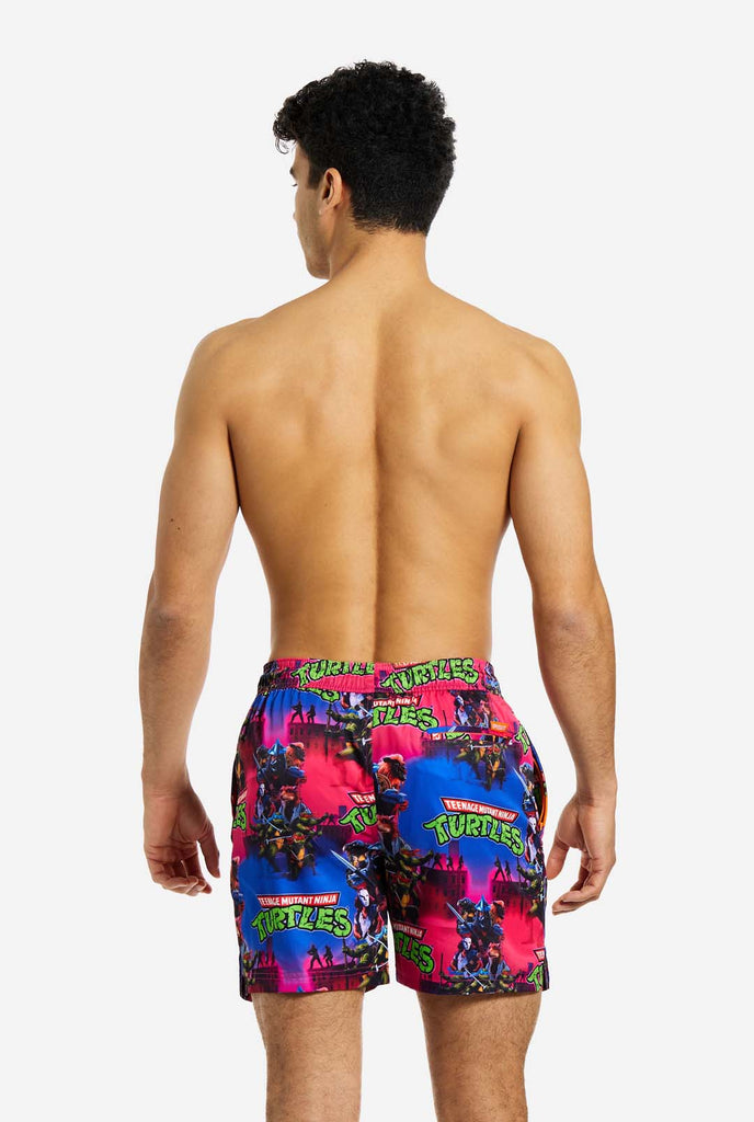 Man wearing TMNT Dude swim trunks for men, view from the back
