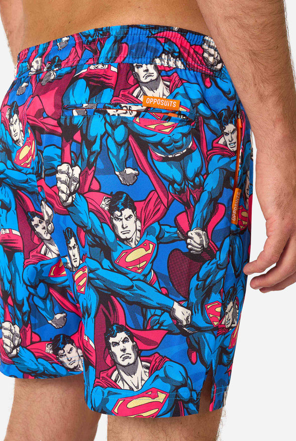 Man wearing a Men's Superman-themed swim shorts featuring a bold comic book design with multiple action poses of the Man of Steel. Perfect for superhero fans looking to make a splash. Close-up from the back.