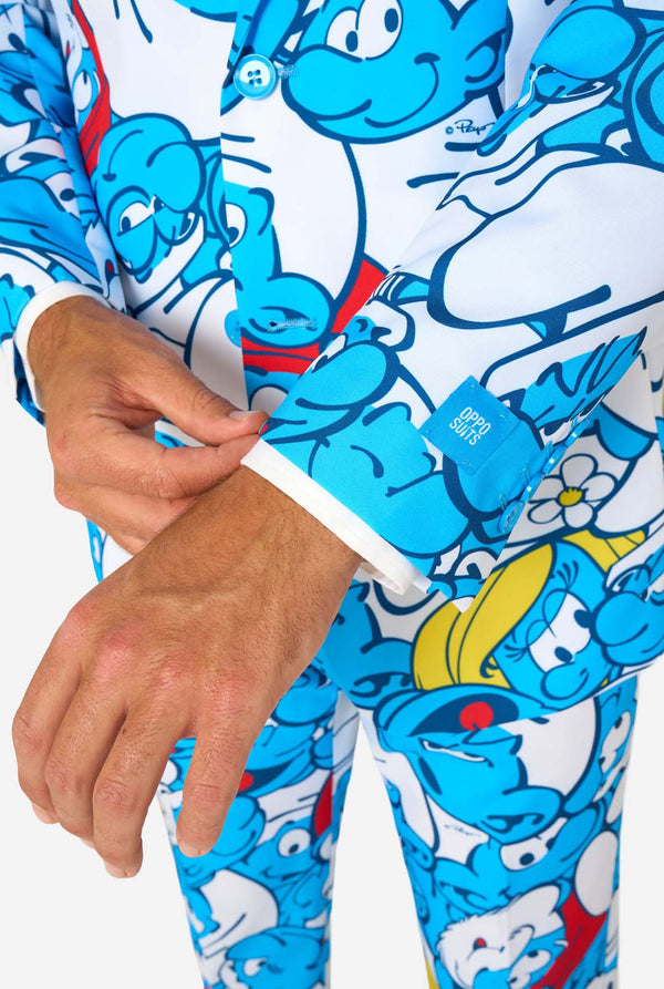 Man wearing a colorful Smurfs men's suit with an all-over cartoon print in blue, white, red, and yellow, including a matching tie and white shirt, standing against a plain background. Sleeves close up.