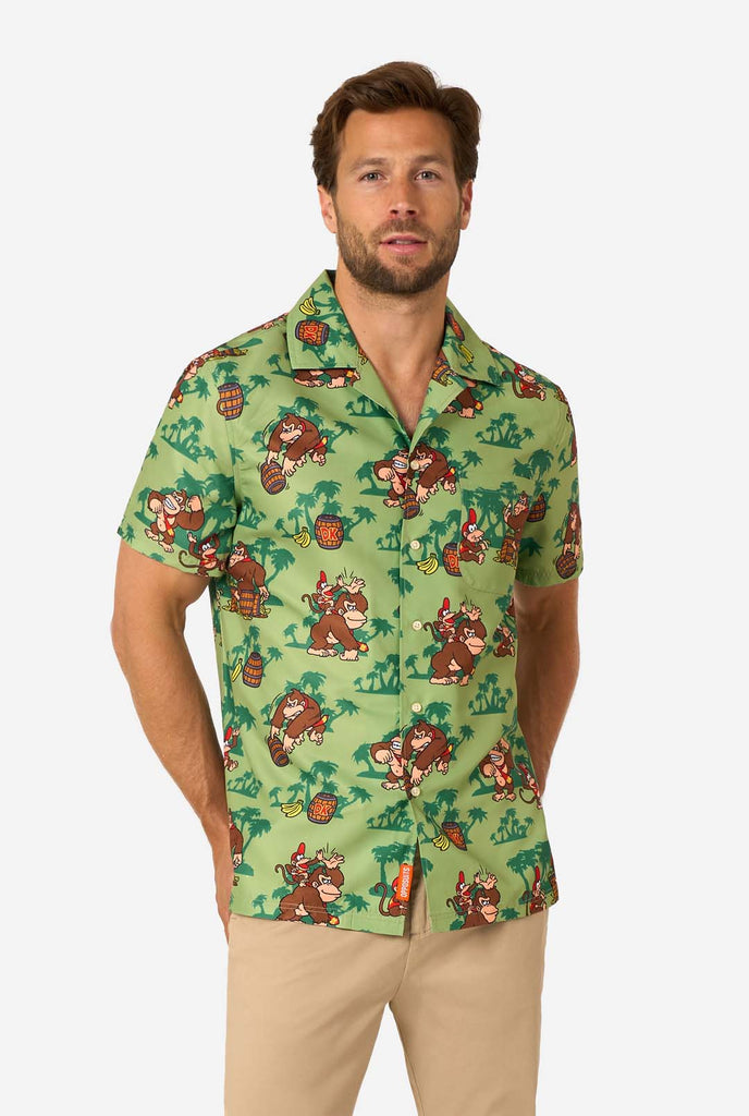 Image of a man wearing a Donkey Kong themed Hawaiian shirt. The shirt has a light green background and contains dark green palm trees, and multiple images of the character Donkey Kong, from Super Mario. The man is looking into the camera.