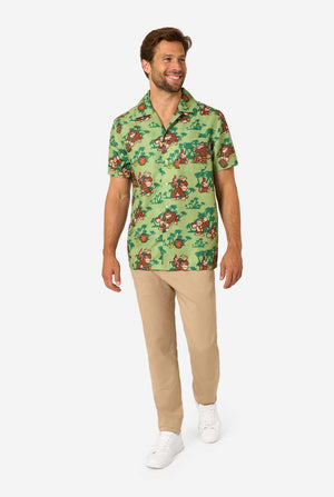 Image of a man wearing a Donkey Kong themed Hawaiian shirt. The shirt has a light green background and contains dark green palm trees, and multiple images of the character Donkey Kong, from Super Mario. The man is looking to the side, full body image.