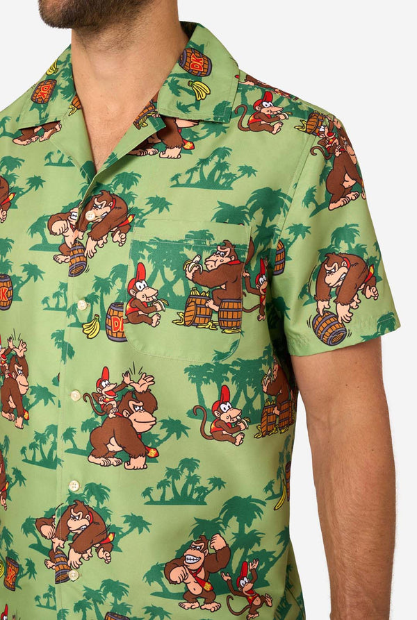 Image of a man wearing a Donkey Kong themed Hawaiian shirt. The shirt has a light green background and contains dark green palm trees, and multiple images of the character Donkey Kong, from Super Mario. Close up of the chest.