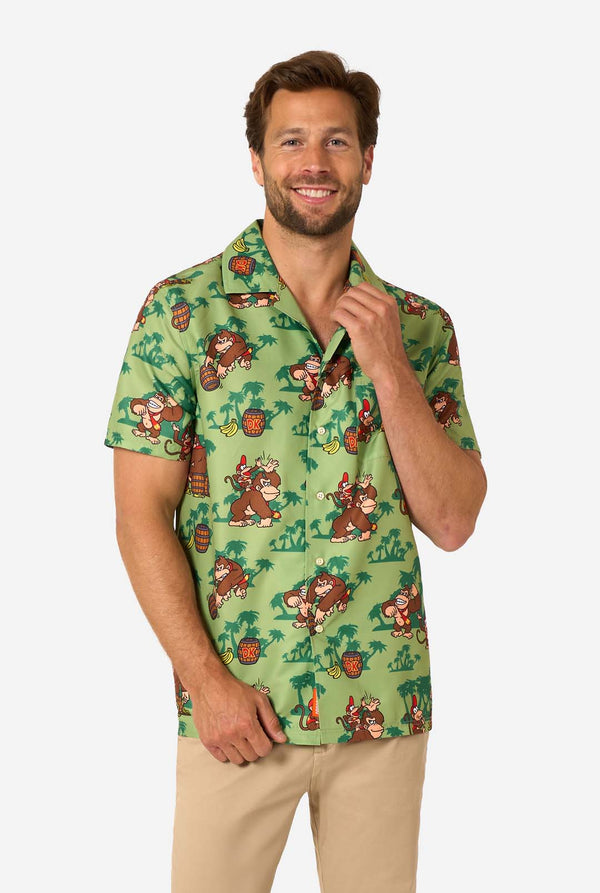 Image of a man wearing a Donkey Kong themed Hawaiian shirt. The shirt has a light green background and contains dark green palm trees, and multiple images of the character Donkey Kong, from Super Mario. The man is looking into the camera.
