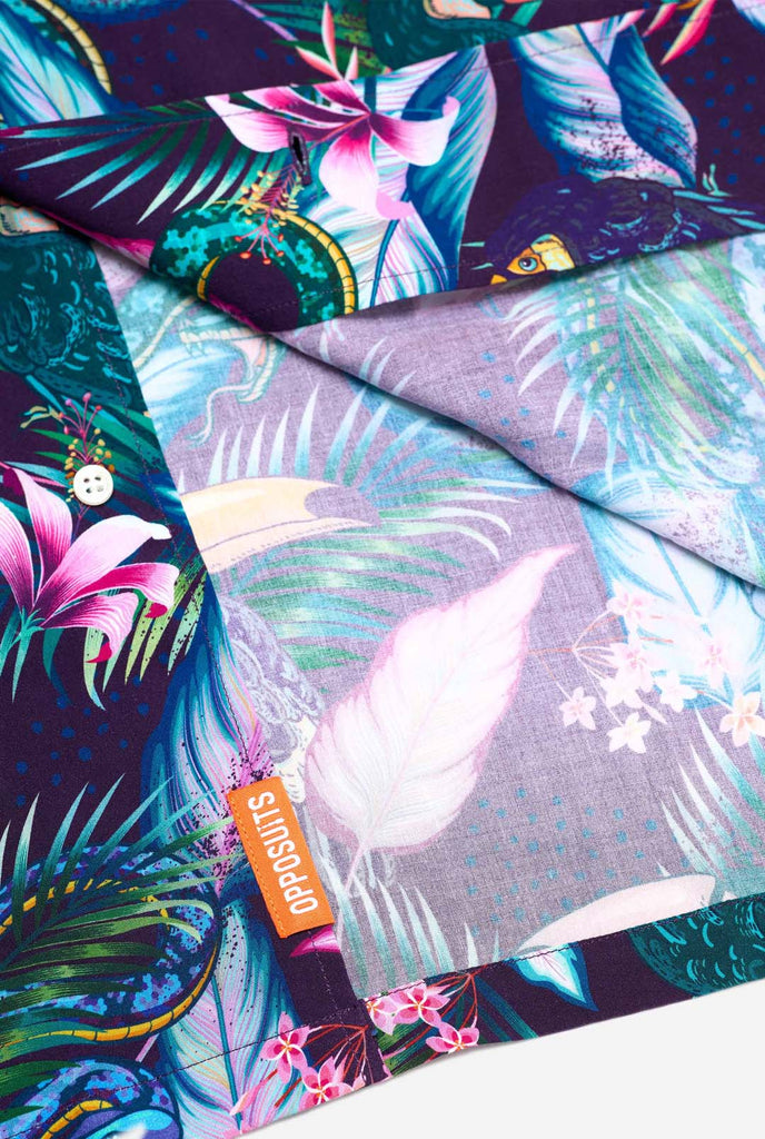 Image of a purple Hawaiian shirt with a tropical print, resembling the jungle night live. Print consists of parrots, snakes, leaves and flowers. Close-up bottom of shirt.
