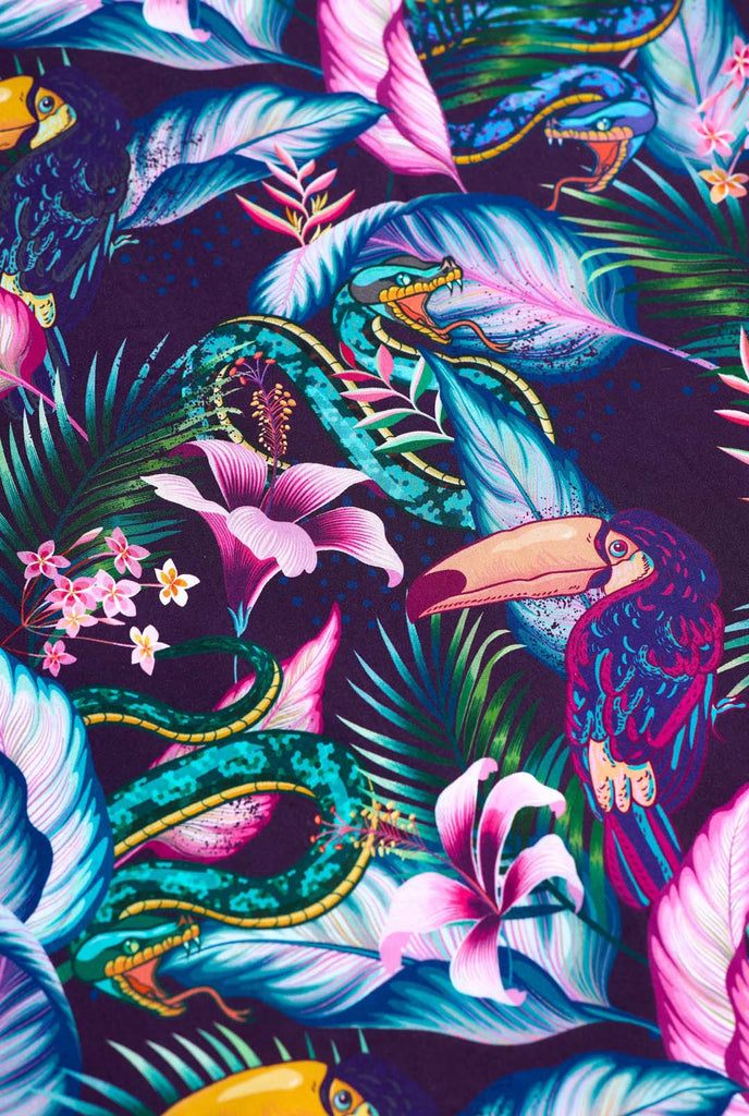 Image of a purple Hawaiian shirt with a tropical print, resembling the jungle night live. Print consists of parrots, snakes, leaves and flowers. Close-up.