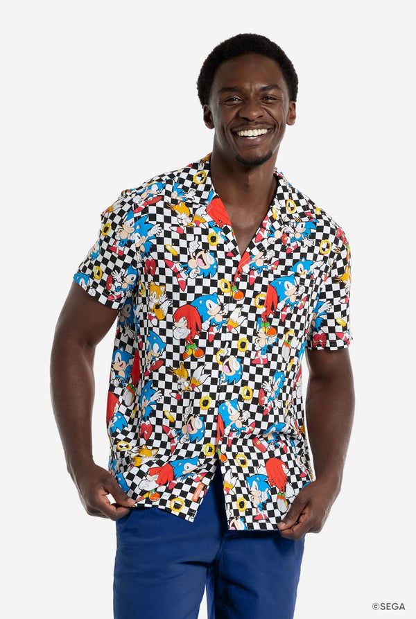 A man is wearing a black and white checkered Hawaiian shirt with characters from the Sonic the Hedgehog franchise and golden rings on it. He is smiling in the camera.