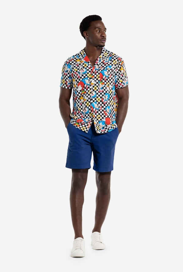 A man is wearing a black and white checkered Hawaiian shirt with characters from the Sonic the Hedgehog franchise and golden rings on it. Hands in his pockets and looking to the side.