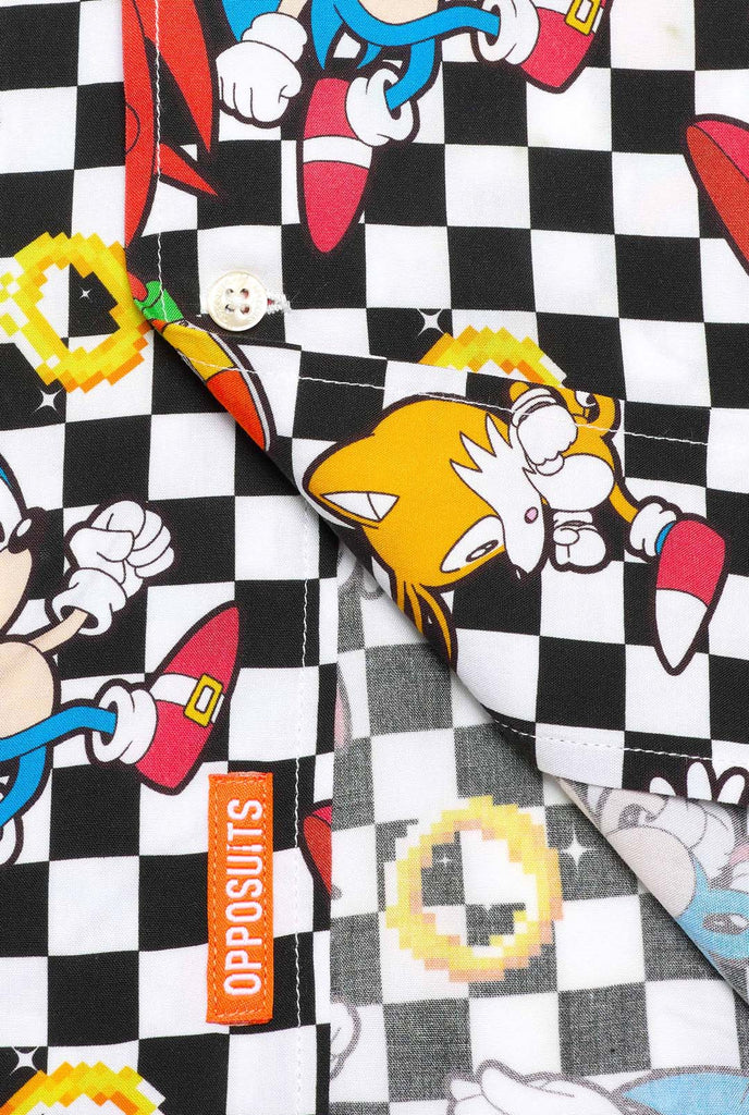 Close up of a black and white checkered Hawaiian shirt with characters from the Sonic the Hedgehog franchise and golden rings on it. Showing the bottom part of the shirt.