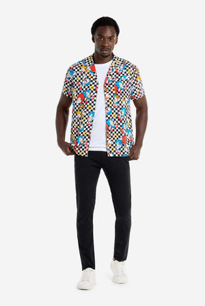 A man is wearing a black and white checkered Hawaiian shirt with characters from the Sonic the Hedgehog franchise and golden rings on it. Also wearing black pants. He is looking in the camera and holding the bottom of the shirt.