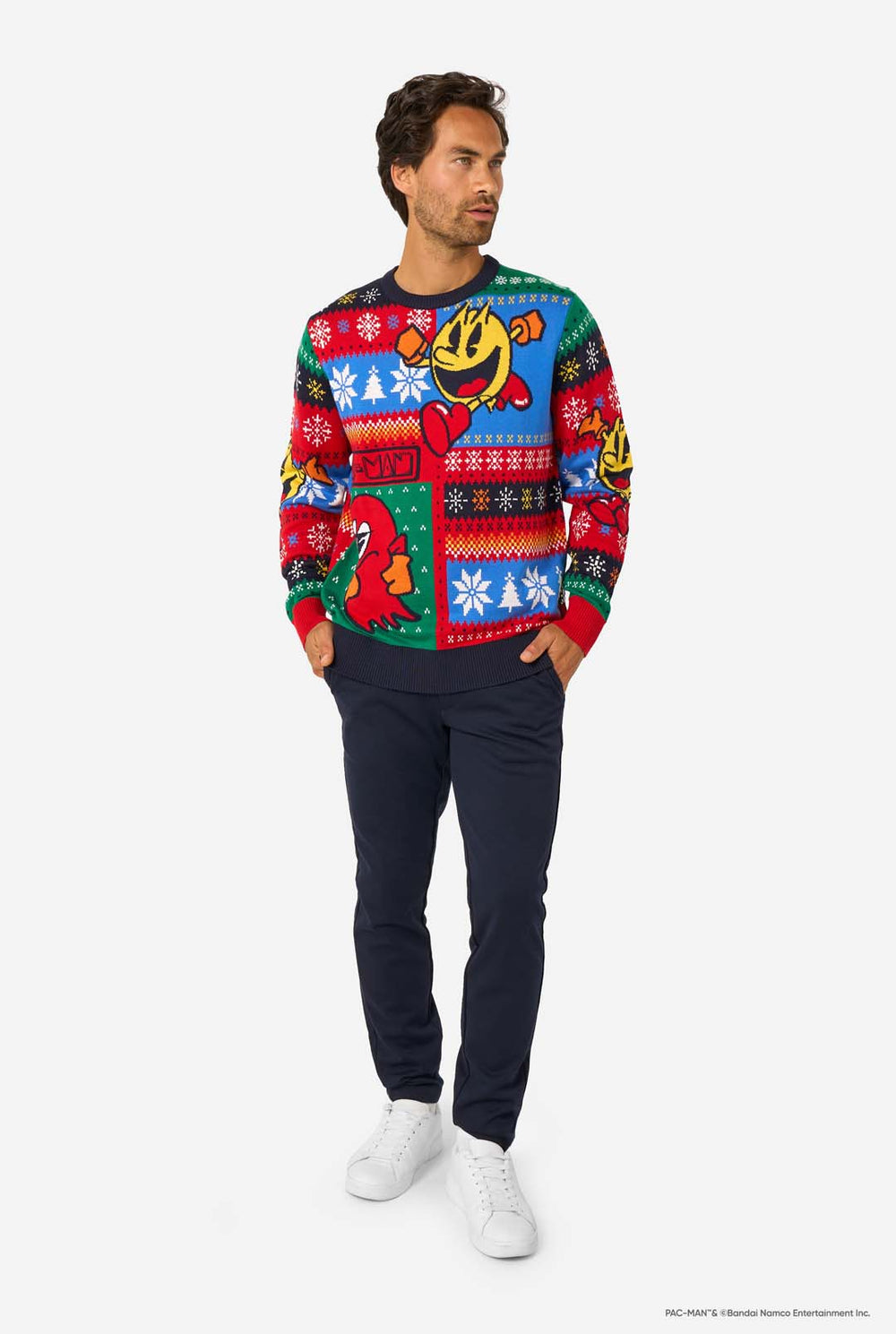 Smiling man wearing a colorful knitted Christmas sweater featuring Pac-Man and a red ghost with festive snowflake patterns.