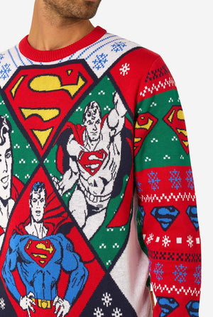 Man wearing a colorful knitted Christmas sweater featuring multiple Superman designs and the iconic “S” logo. Close-up.