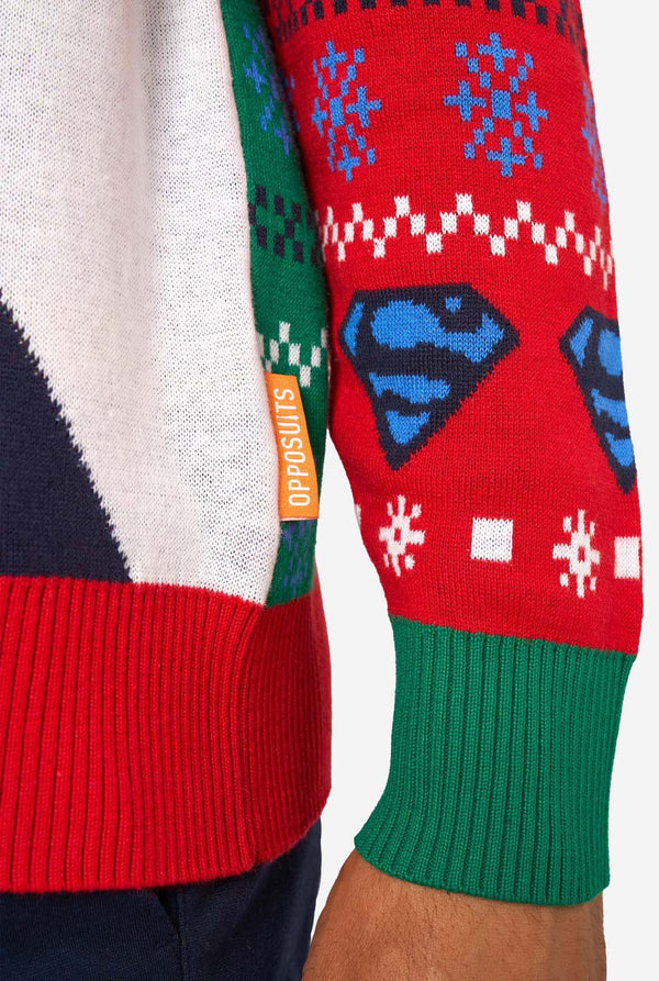 Man wearing a colorful knitted Christmas sweater featuring multiple Superman designs and the iconic “S” logo. Sleeve close up.