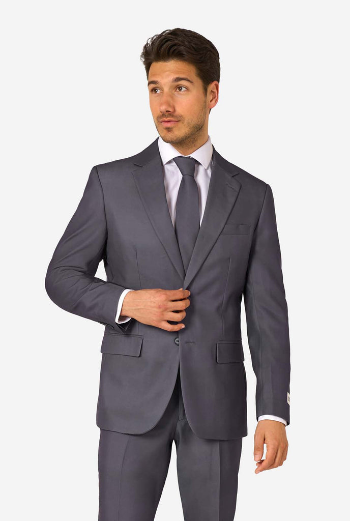 A man is wearing a stylish charcoal colored grey suit with a white dress shirt, looking confidently. Perfect formal outfit for men's special occasions, weddings, and parties. Looking side ways.