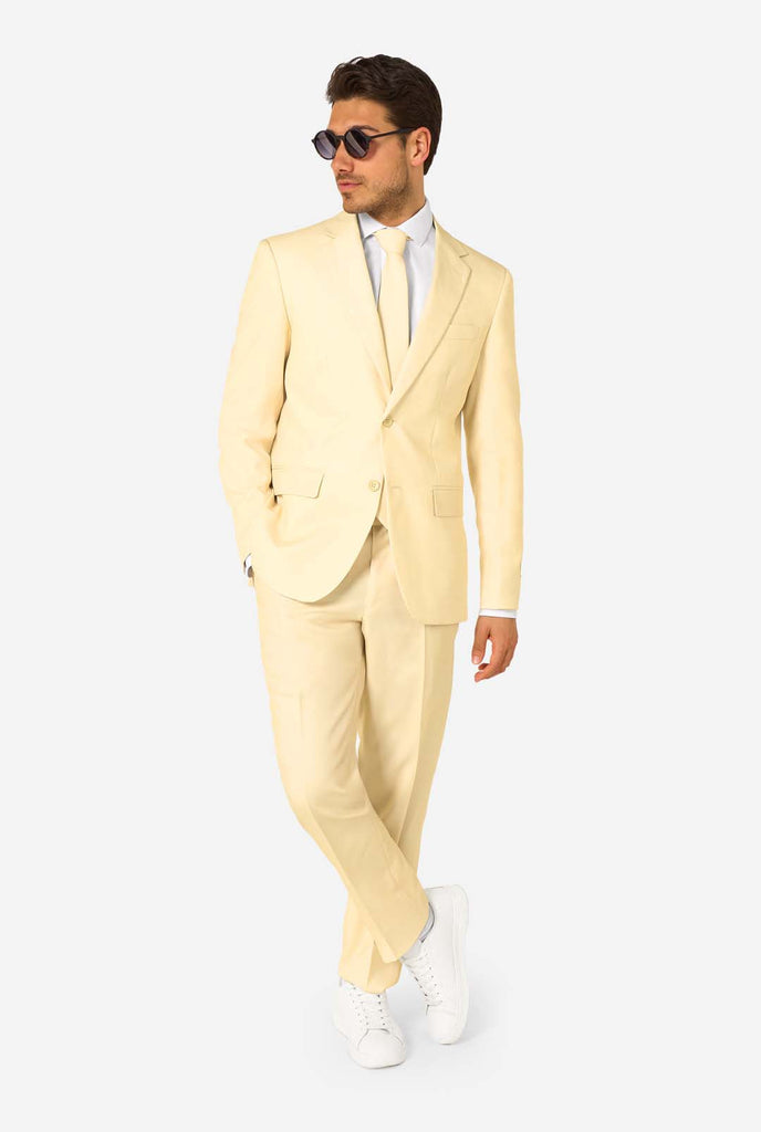 Elegant men's suit in a soft pastel yellow shade, perfect for weddings, summer events, and formal occasions. This stylish tailored suit features a slim fit design, notch lapels, and a matching tie for a sophisticated look. Ideal for modern gentlemen looking to make a statement with a light-colored pastel suit. Also wearing sunglasses.