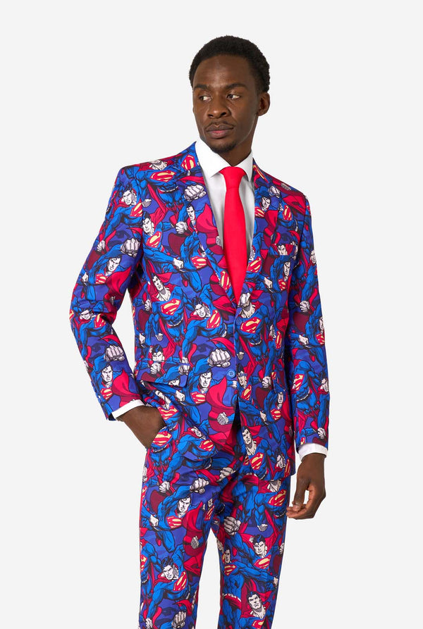 A man wearing a Superman themed suit with a red tie and a white shirt on a white background.