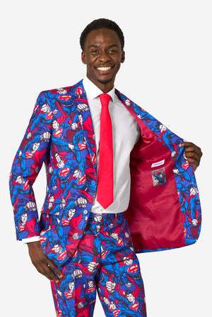 A man wearing a Superman themed suit with a red tie and a white shirt on a white background. Holding his jacket open