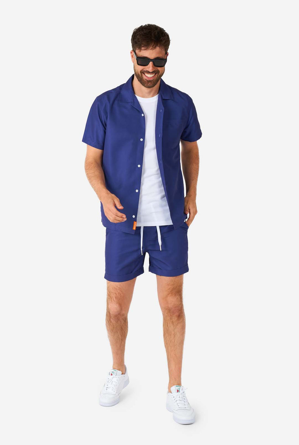 Man wearing blue summer set consisting of shirt and shorts and wearing sunglasses.