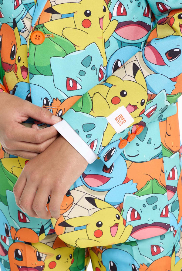 Teen wearing formal multi color suit with all-over Pokemon print. The suit contains the characters Pikachu, Bulbasaur, Charmander and Squirtle.