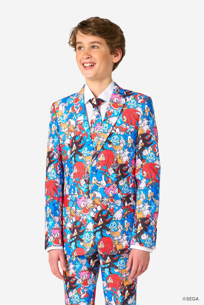 Teen boy wearing a vibrant Sonic teen suit featuring colorful prints of Sonic the Hedgehog characters including Sonic, Knuckles, Tails, and Amy, paired with a matching tie and white shirt.
