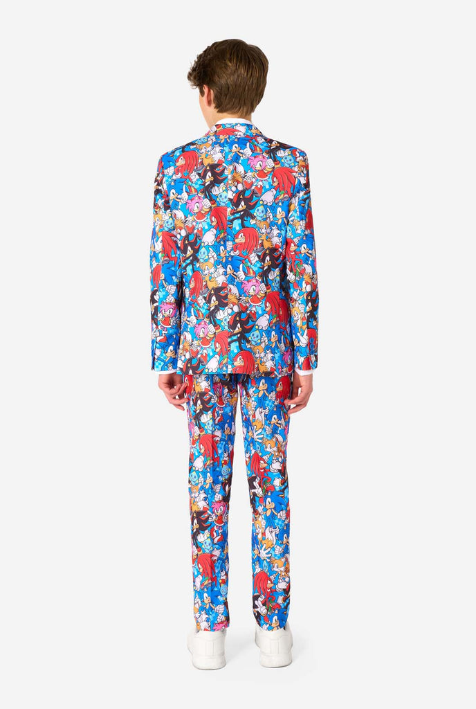 Teen boy wearing a vibrant Sonic teen suit featuring colorful prints of Sonic the Hedgehog characters including Sonic, Knuckles, Tails, and Amy, paired with a matching tie and white shirt. View from the back.