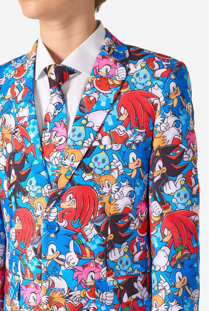 Teen boy wearing a vibrant Sonic teen suit featuring colorful prints of Sonic the Hedgehog characters including Sonic, Knuckles, Tails, and Amy, paired with a matching tie and white shirt. Chest close up.