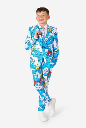 Teen boy wearing a vibrant Smurfs kids suit with colorful cartoon character prints in blue, red, yellow, and white, paired with a matching tie and white shirt, smiling against a plain background. Full body image.
