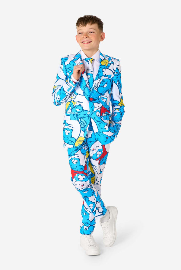 Teen boy wearing a vibrant Smurfs kids suit with colorful cartoon character prints in blue, red, yellow, and white, paired with a matching tie and white shirt, smiling against a plain background. Full body image.
