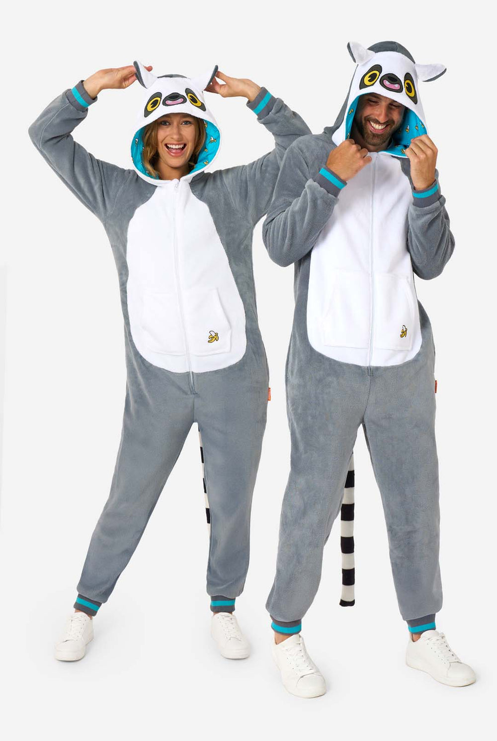 A man and women are wearing a grey and white lemur adult onesie featuring playful hood details and cozy, soft material, perfect for lounging or costume events. Including black and white tail. The hood are on their heads.