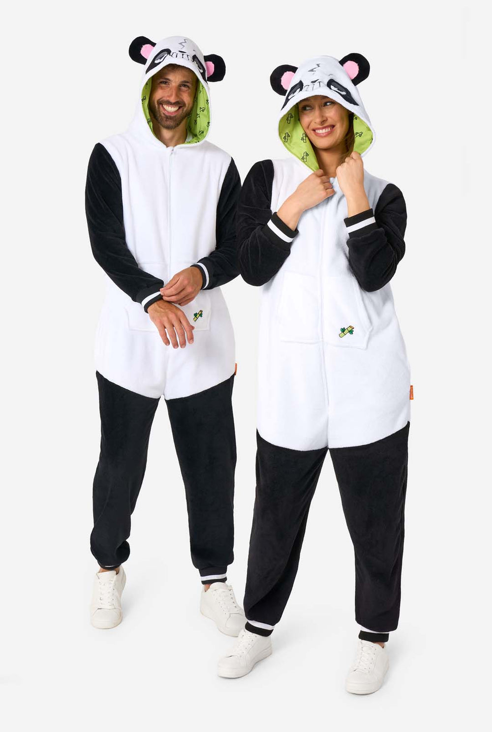 A man and woman are wearing a panda-themed adult onesie. This cozy onesie features black and white panda colors with a playful hood showcasing panda ears and a cute face. Perfect for lounging or fun costume occasions. 