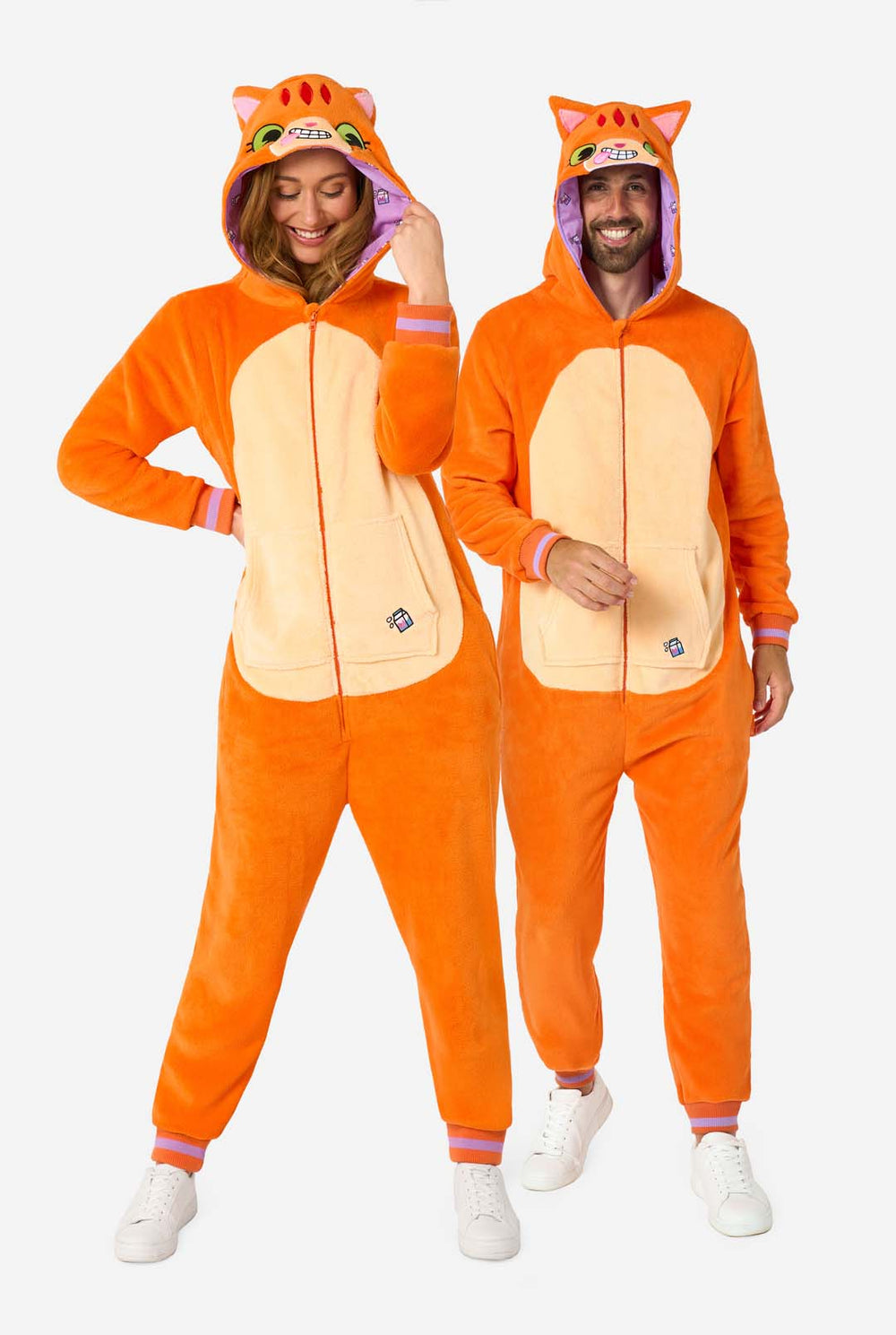 A man and women are wearing an orange adult onesie designed as a red cat onesie. The onesie features a hood resembling a cat's head, and cat details, perfect for cozy lounging or costume parties. Both have the hood on their head.