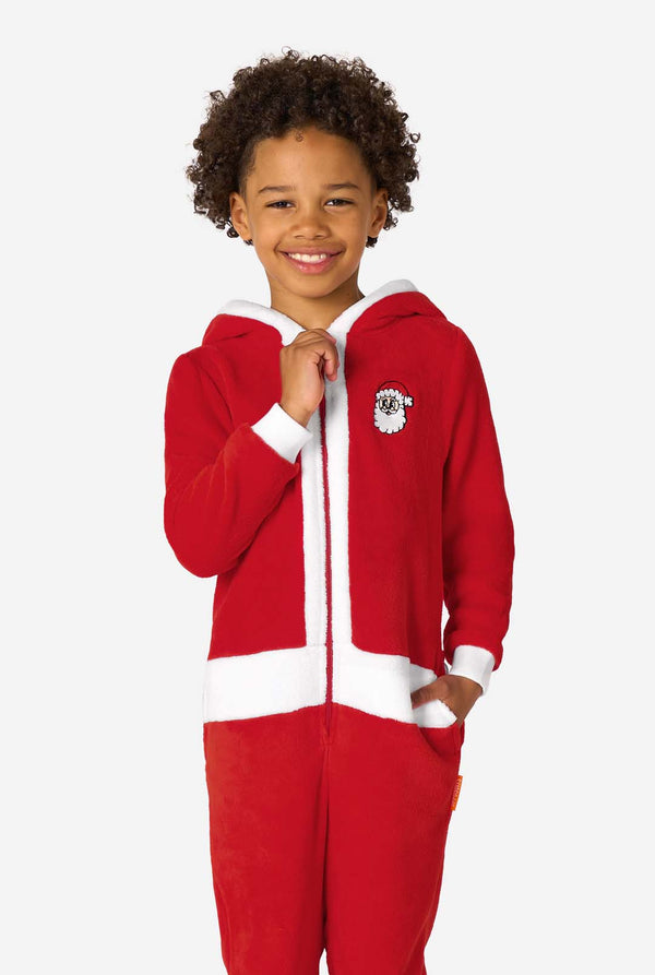 Child smiling while wearing a red Santa onesie with white trim, one hand holding the collar.