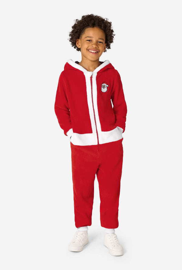 Full-body view of a child standing and smiling in a red Santa onesie with white trim and white sneakers.